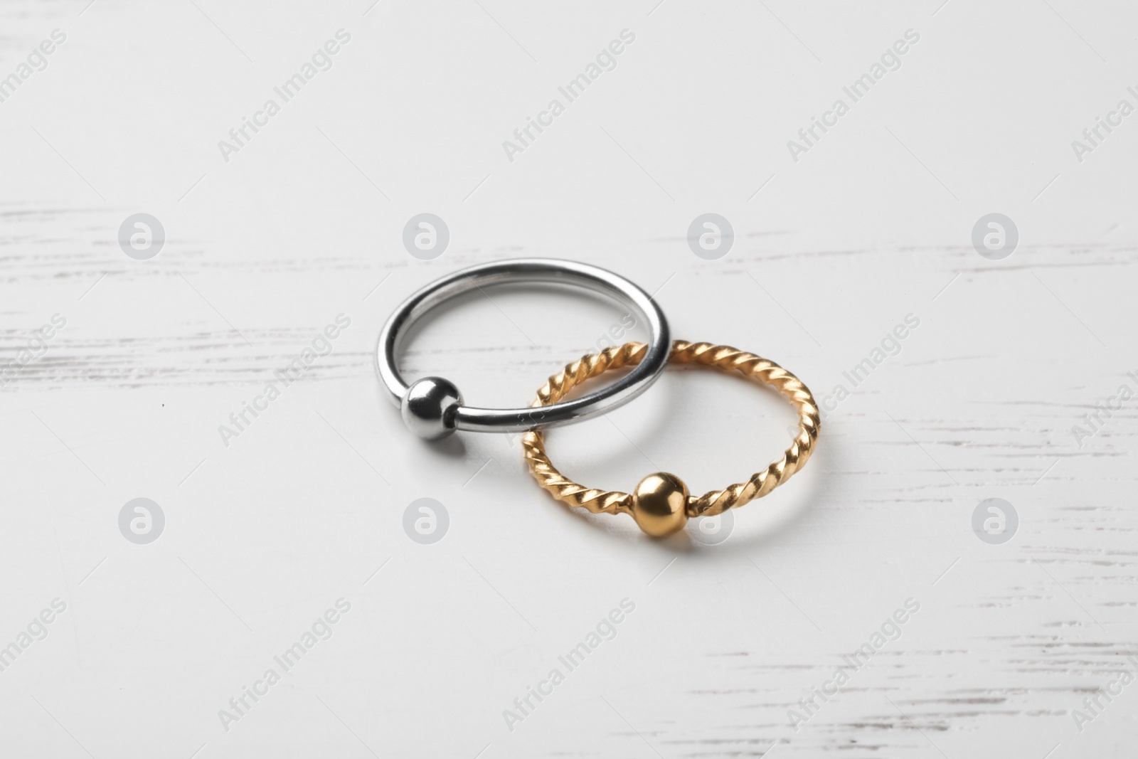 Photo of Stylish captive bead rings on white wooden table. Piercing jewelry