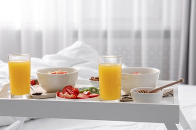 Photo of Tasty breakfast served in bed. Oatmeal, juice, fruits and honey on tray