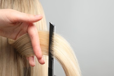 Photo of Hairdresser combing and cutting client's hair on light grey background, closeup. Space for text