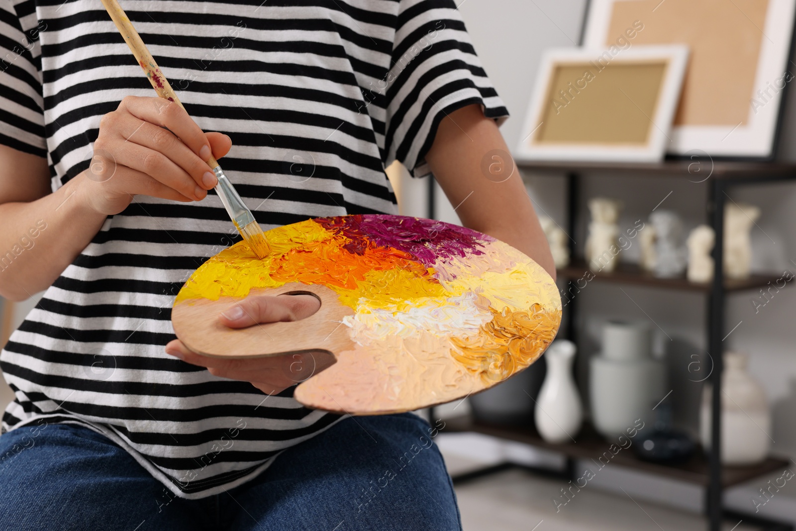 Photo of Young woman mixing paints on palette with brush in studio, closeup