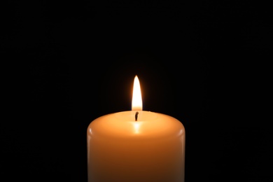 Photo of Wax candle burning on black background, closeup