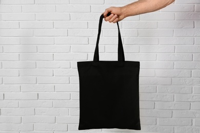 Man holding cotton shopping eco bag against brick wall. Mockup for design