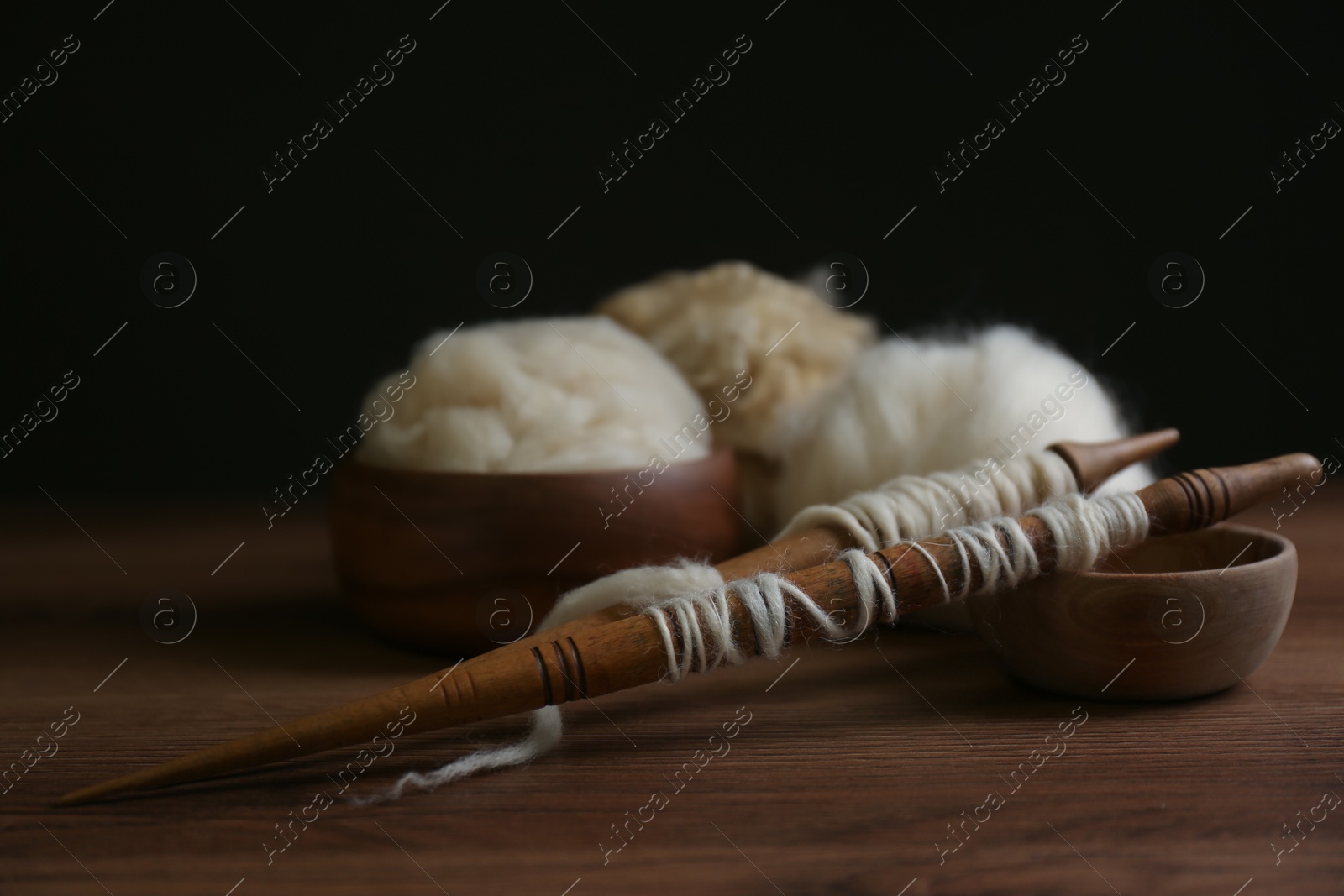 Photo of Spindles and soft white wool on wooden table, space for text