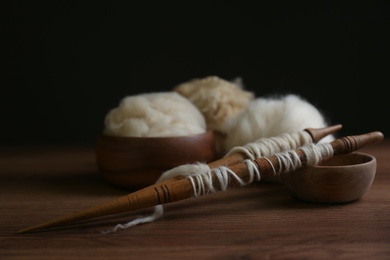 Spindles and soft white wool on wooden table, space for text