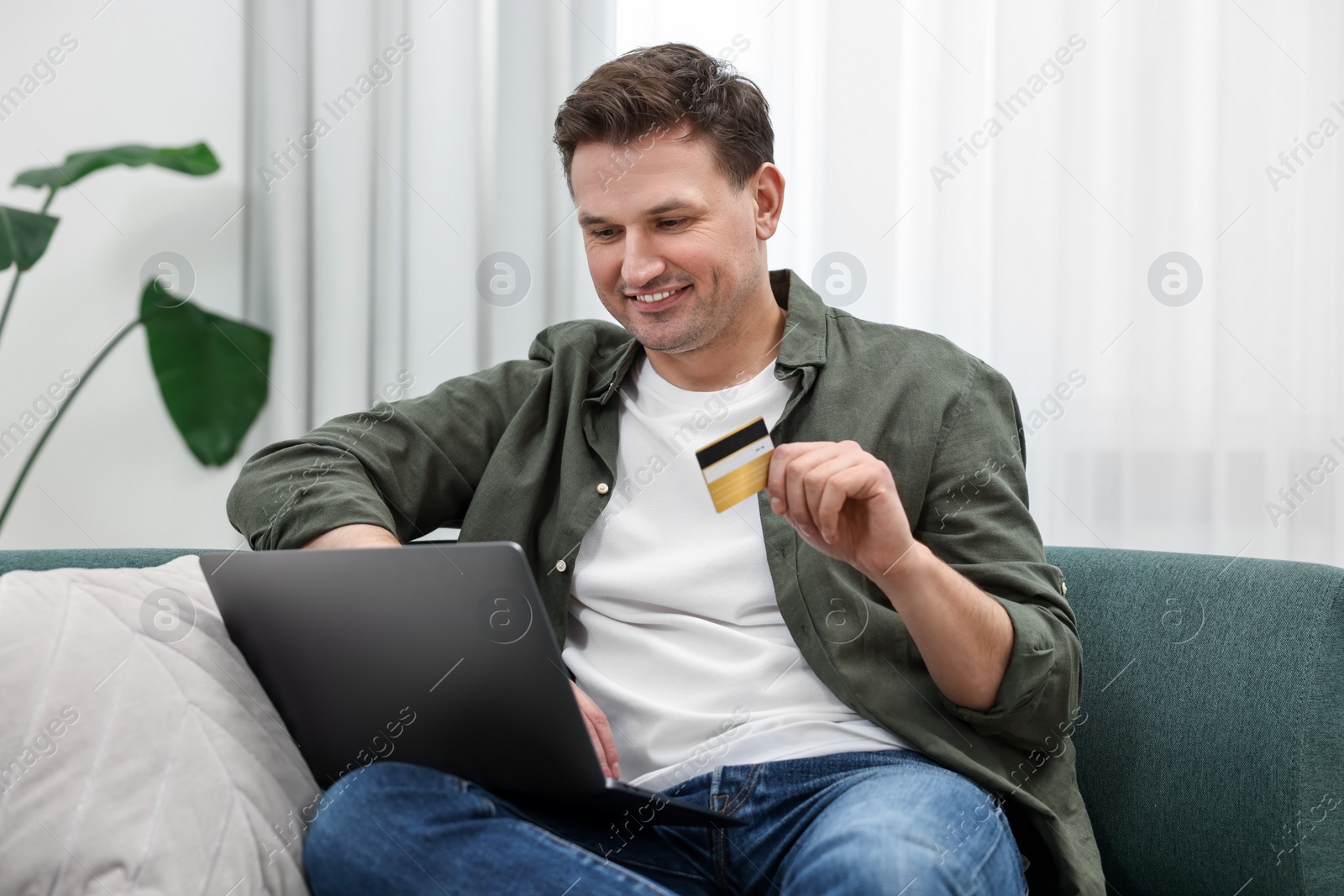 Photo of Happy man with credit card using laptop for shopping online on sofa at home