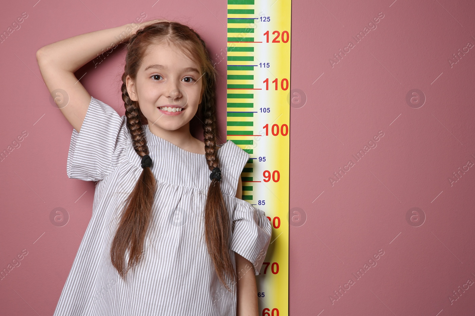 Photo of Little girl measuring her height on color background