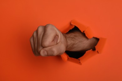 Photo of Man breaking through orange paper with fist, closeup