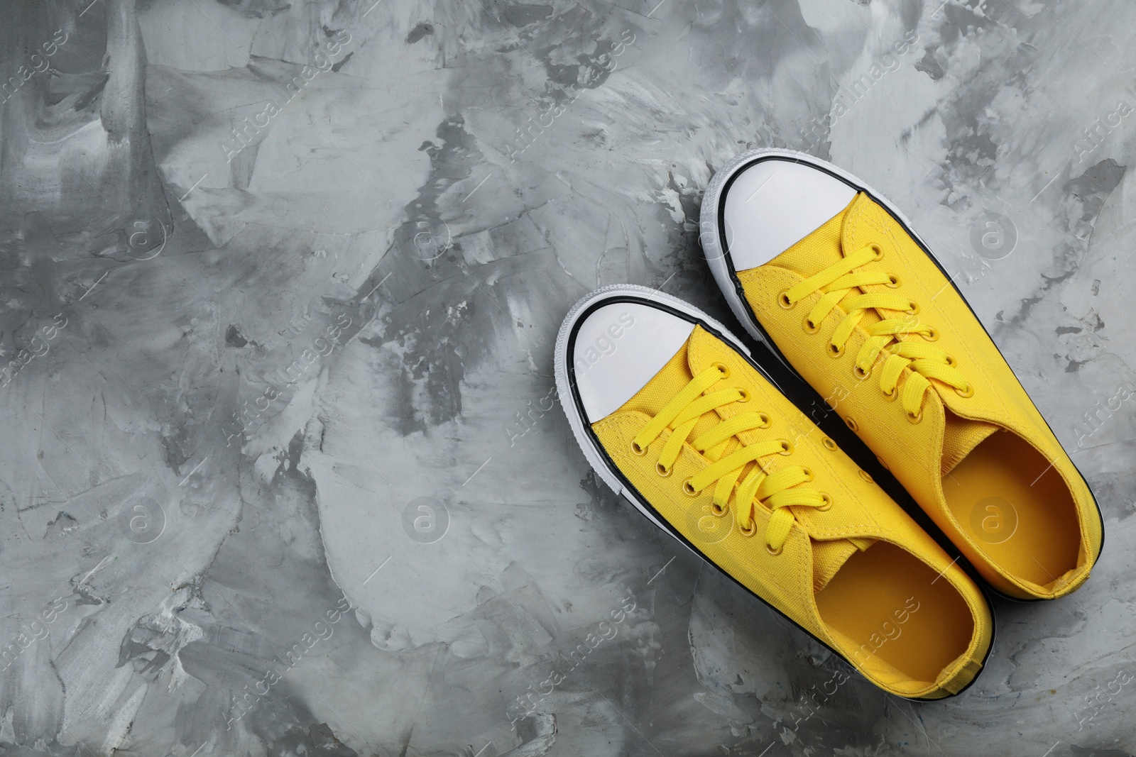 Photo of Pair of yellow sneakers on grey stone table, flat lay. Space for text