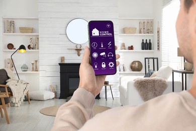 Man using smart home control system via application on mobile phone indoors, closeup
