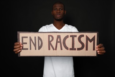 Photo of African American man holding sign with phrase End Racism on black background
