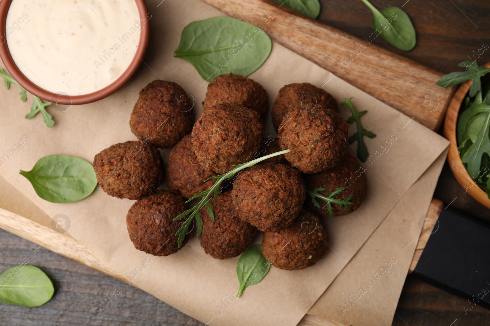 Photo of Delicious falafel balls, arugula, basil and sauce on wooden table, top view