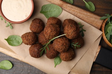 Photo of Delicious falafel balls, arugula, basil and sauce on wooden table, top view