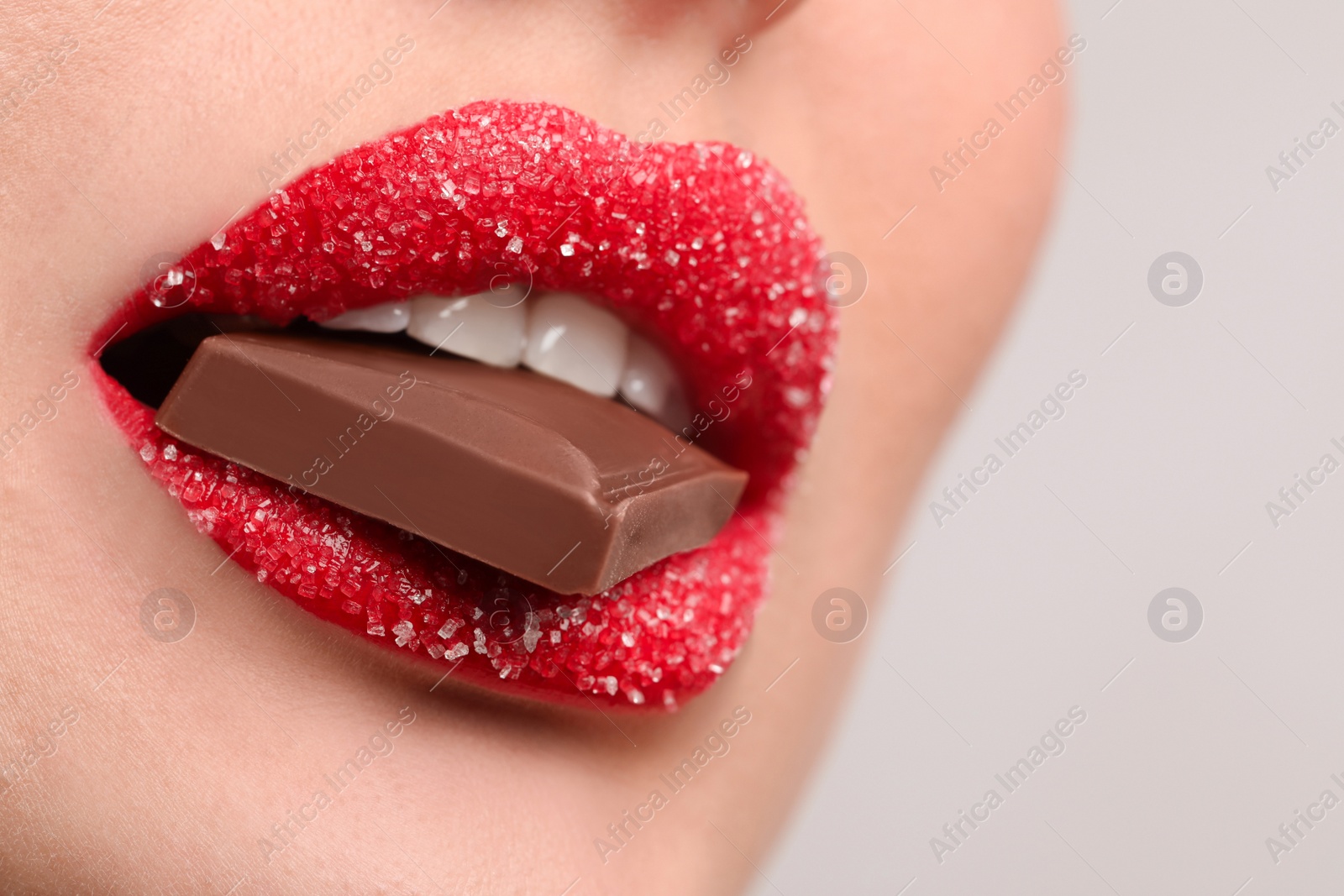 Photo of Closeup view of young woman with beautiful lips covered in sugar eating chocolate on light grey background