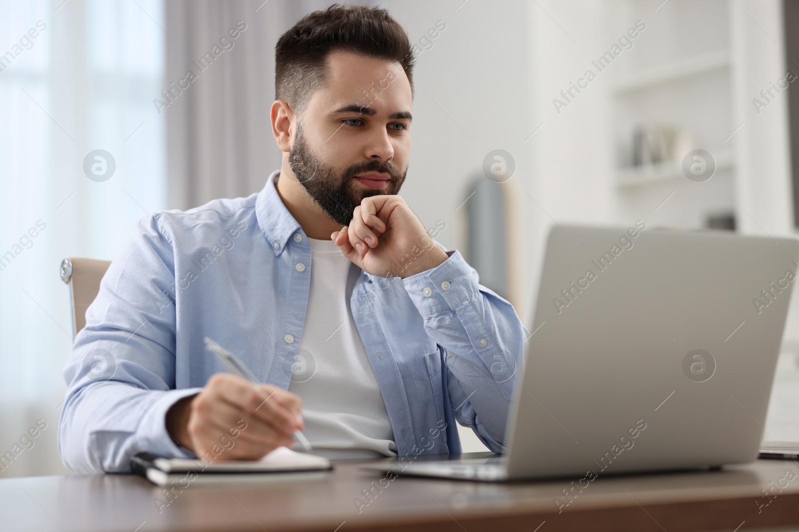 Photo of Young man watching webinar at table in room