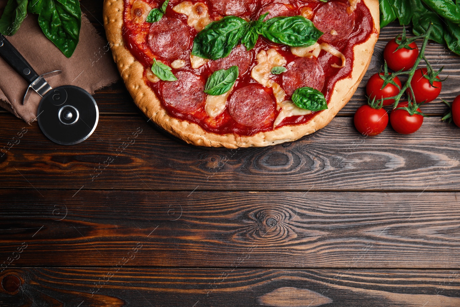 Photo of Pita pizza with pepperoni, cheese, basil and tomatoes on wooden table, flat lay. Space for text