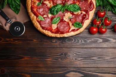 Photo of Pita pizza with pepperoni, cheese, basil and tomatoes on wooden table, flat lay. Space for text