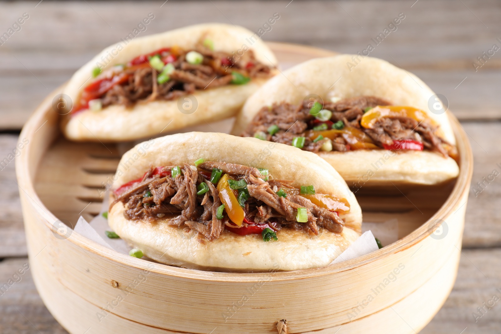 Photo of Delicious gua bao in bamboo steamer on wooden table, closeup