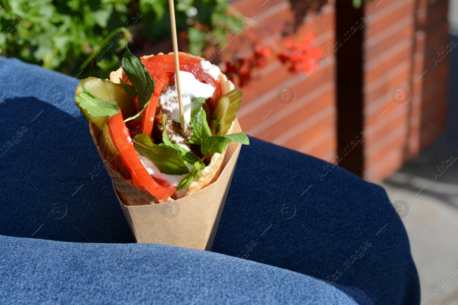 Photo of Woman holding wafer with falafel and vegetables outdoors, closeup. Street food