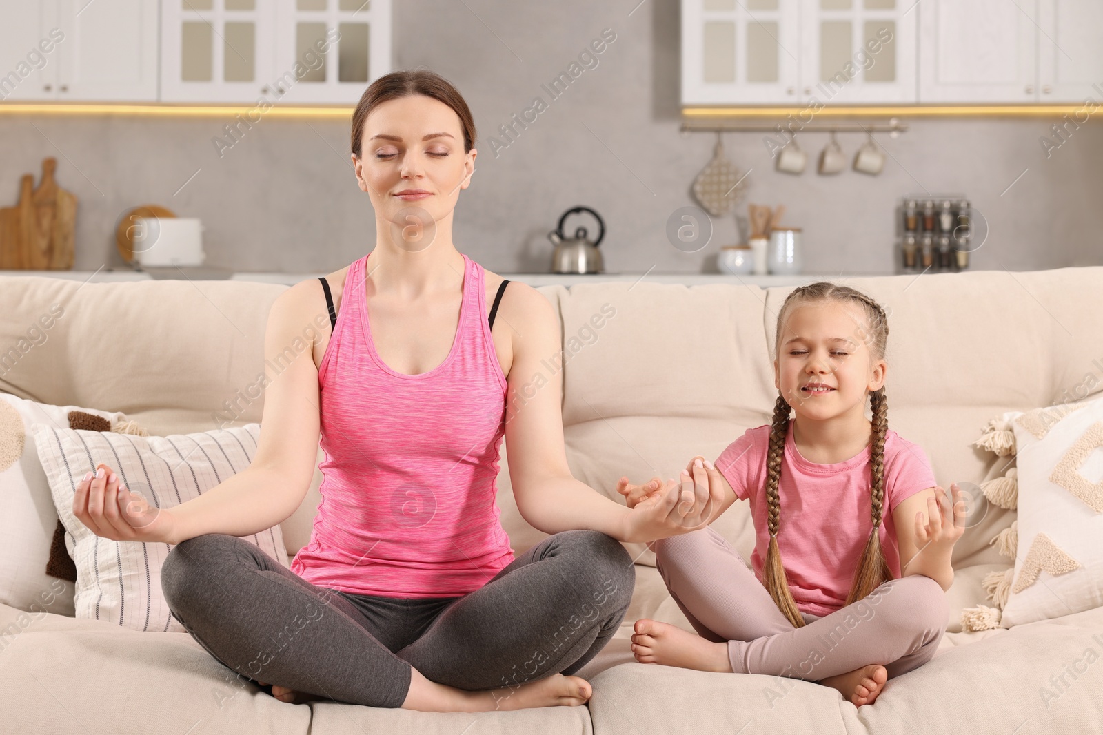 Photo of Mother with daughter meditating on sofa at home. Harmony and zen