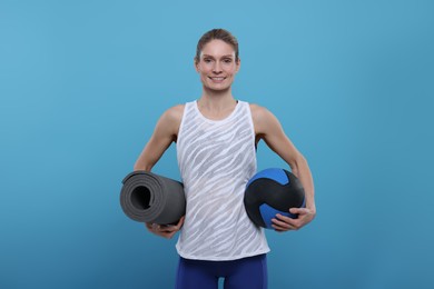Photo of Sportswoman with medicine ball and fitness mat on light blue background, space for text