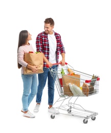 Photo of Young couple with full shopping cart and paper bags on white background