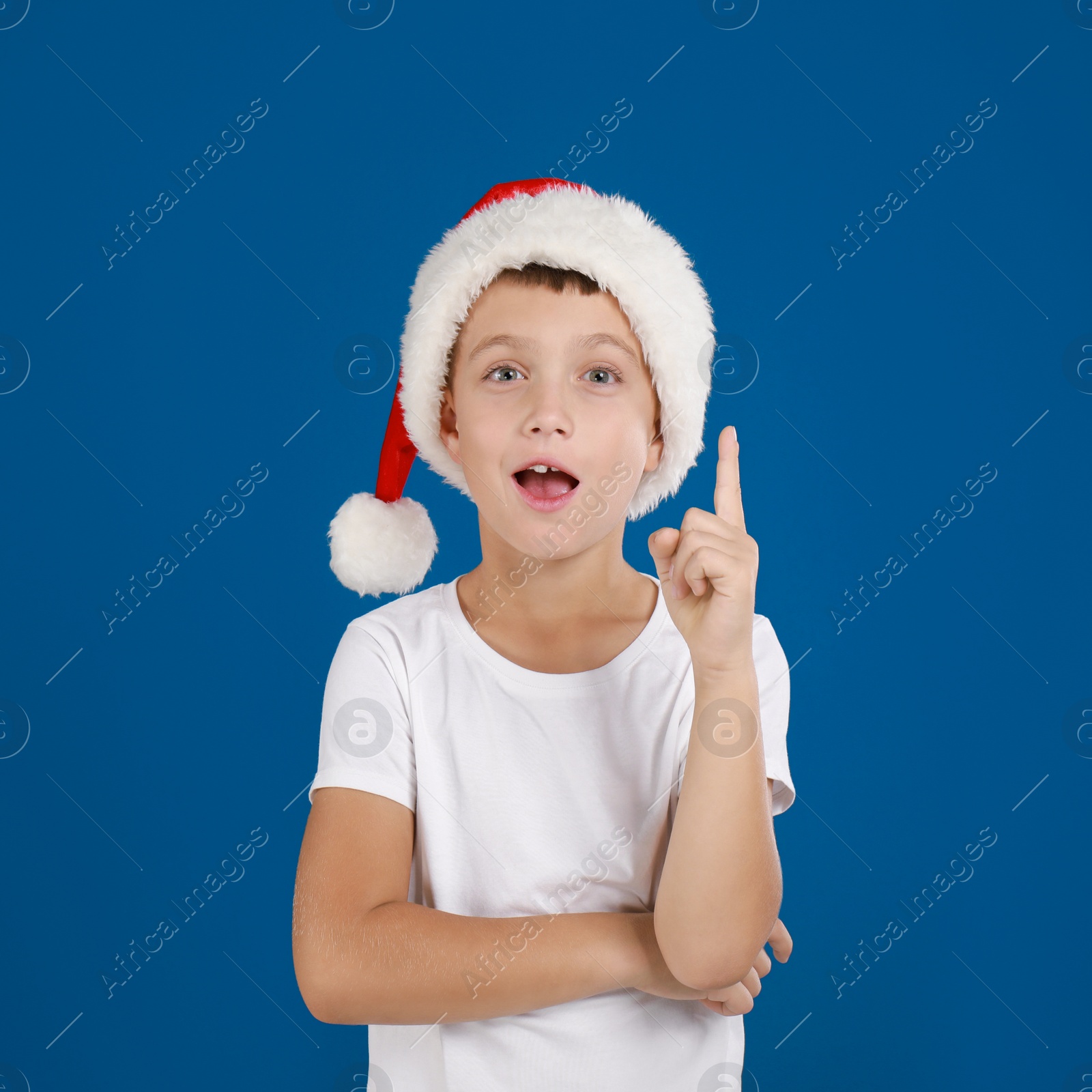 Image of Happy little child in Santa hat on blue background. Christmas celebration