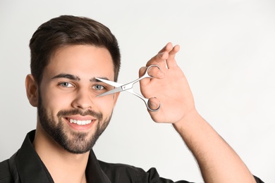 Young hairstylist holding professional scissors on light background