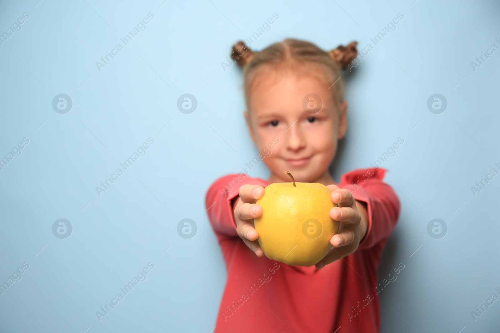 Photo of Cute little girl with yellow apple against light blue background, space for text. Focus on fruit