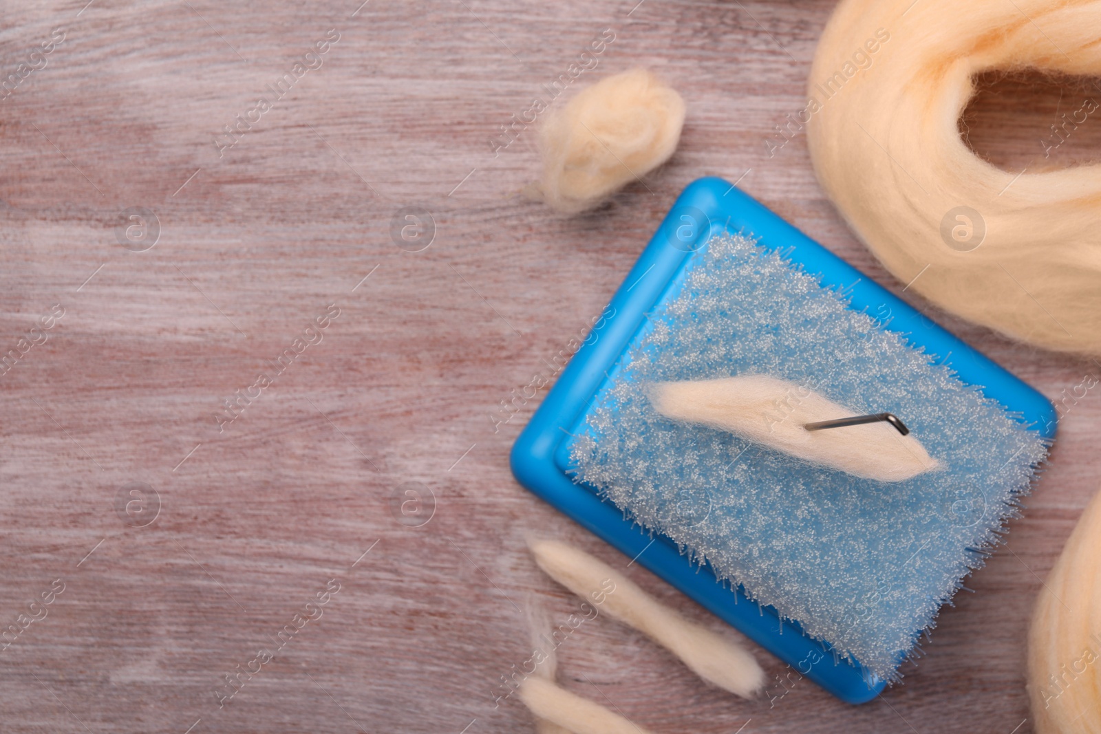 Photo of Felting tools and wool on wooden table, flat lay. Space for text