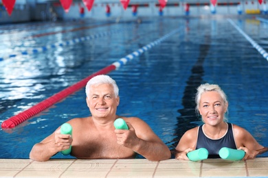 Photo of Sportive senior couple with swimming noodles in indoor pool