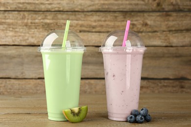 Photo of Plastic cups with different tasty smoothies and fresh fruits on wooden table