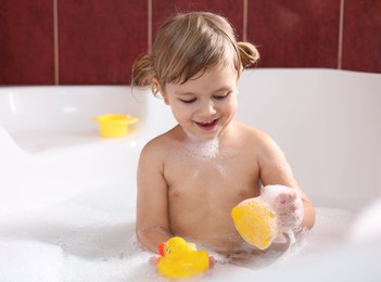 Photo of Smiling girl bathing with toy ducks in tub