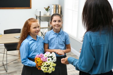 Photo of Schoolgirls with bouquet congratulating their pedagogue in classroom. Teacher's day