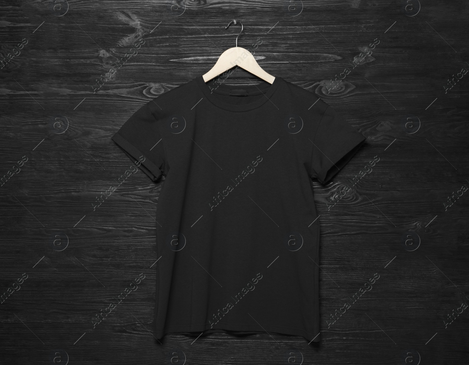 Photo of Hanger with stylish T-shirt on black wooden wall
