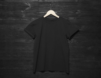 Hanger with stylish T-shirt on black wooden wall
