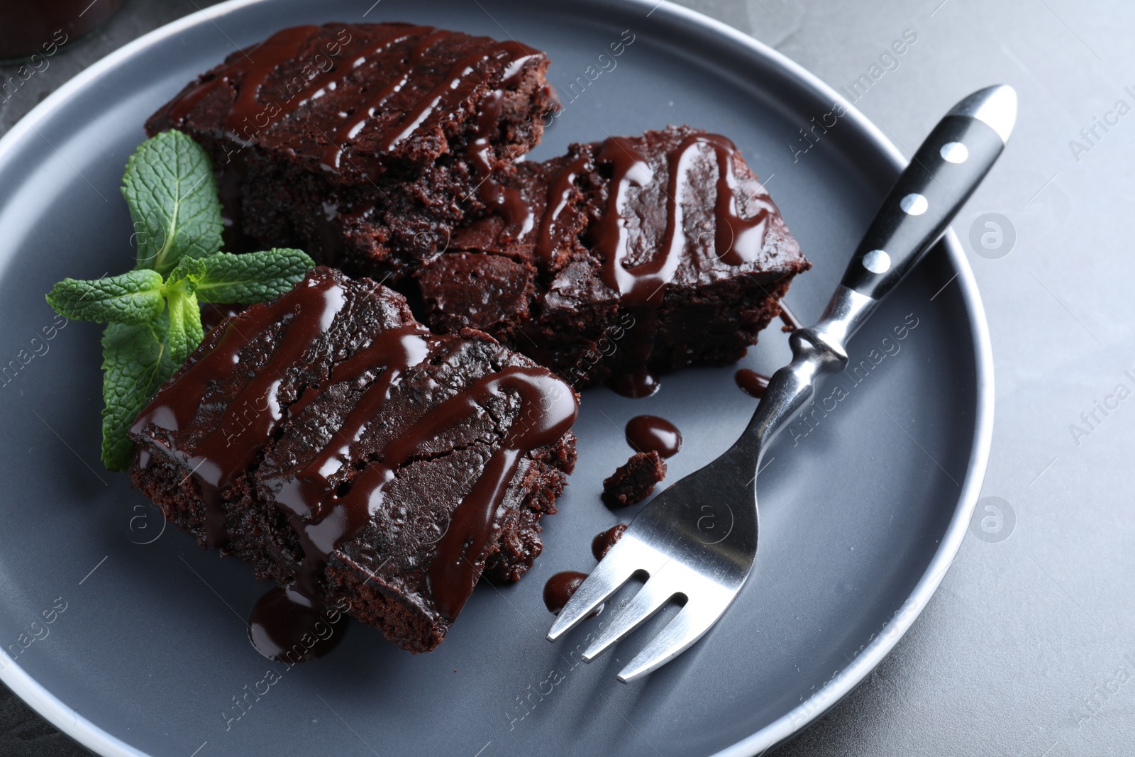 Photo of Delicious chocolate brownies with sweet syrup and mint served on grey table, closeup