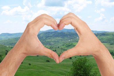 Image of Man making heart with hands outdoors on sunny day, closeup