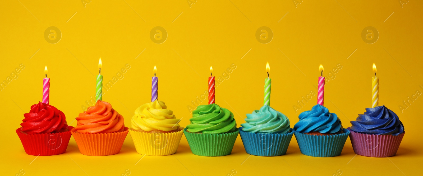 Photo of Delicious birthday cupcakes with burning candles on yellow background