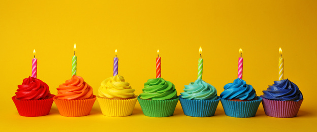 Delicious birthday cupcakes with burning candles on yellow background