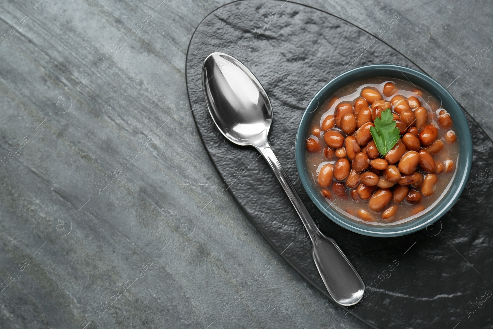 Photo of Tasty canned kidney beans with parsley served on grey table, top view. Space for text