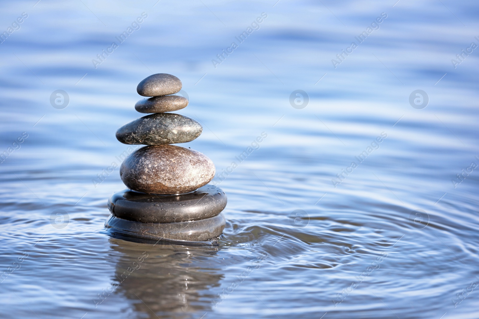 Photo of Stack of dark stones in sea water, space for text. Zen concept