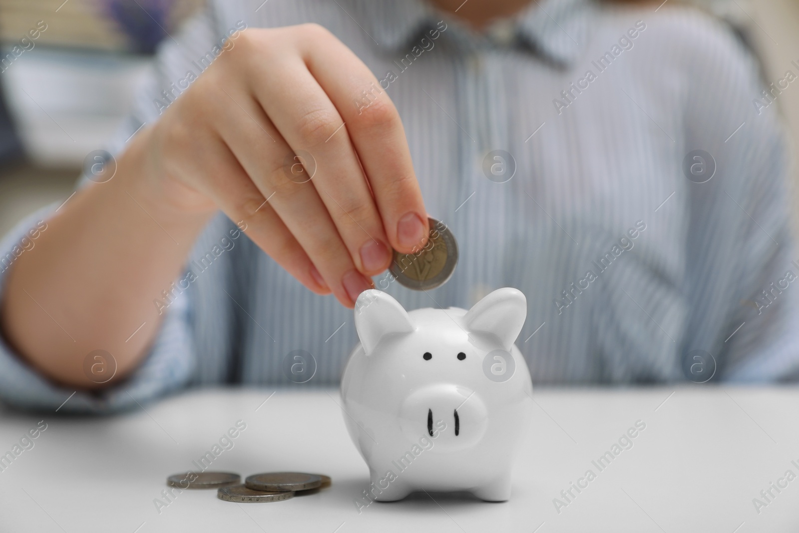 Photo of Woman putting coin into ceramic piggy bank at white wooden table, closeup. Financial savings