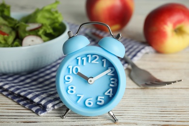 Photo of Alarm clock and healthy food on white wooden table, closeup. Meal timing concept