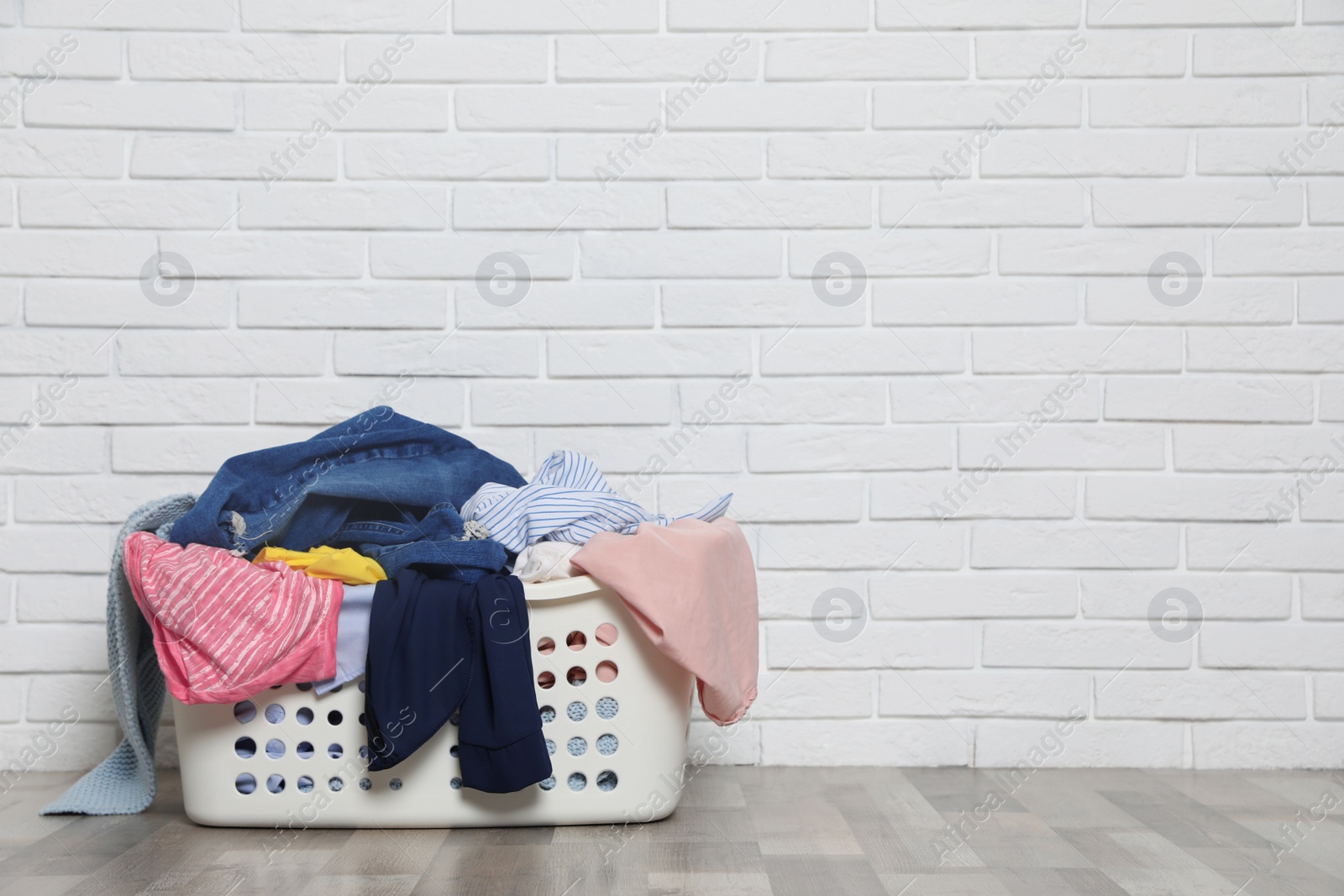 Photo of Laundry basket with dirty clothes on floor near brick wall. Space for text