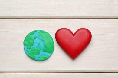 Photo of Happy Earth Day. Plasticine planet and decorative heart on white wooden table, flat lay
