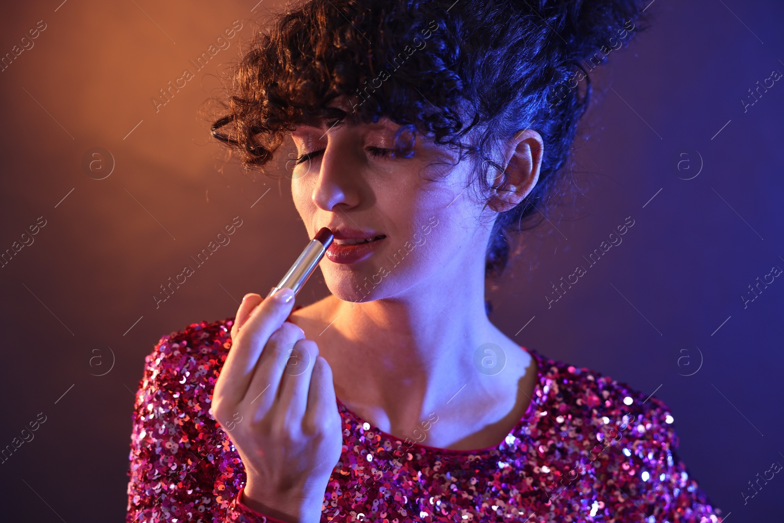Photo of Beautiful young woman with lipstick posing on color background in neon lights