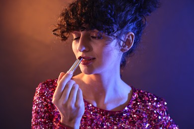 Beautiful young woman with lipstick posing on color background in neon lights