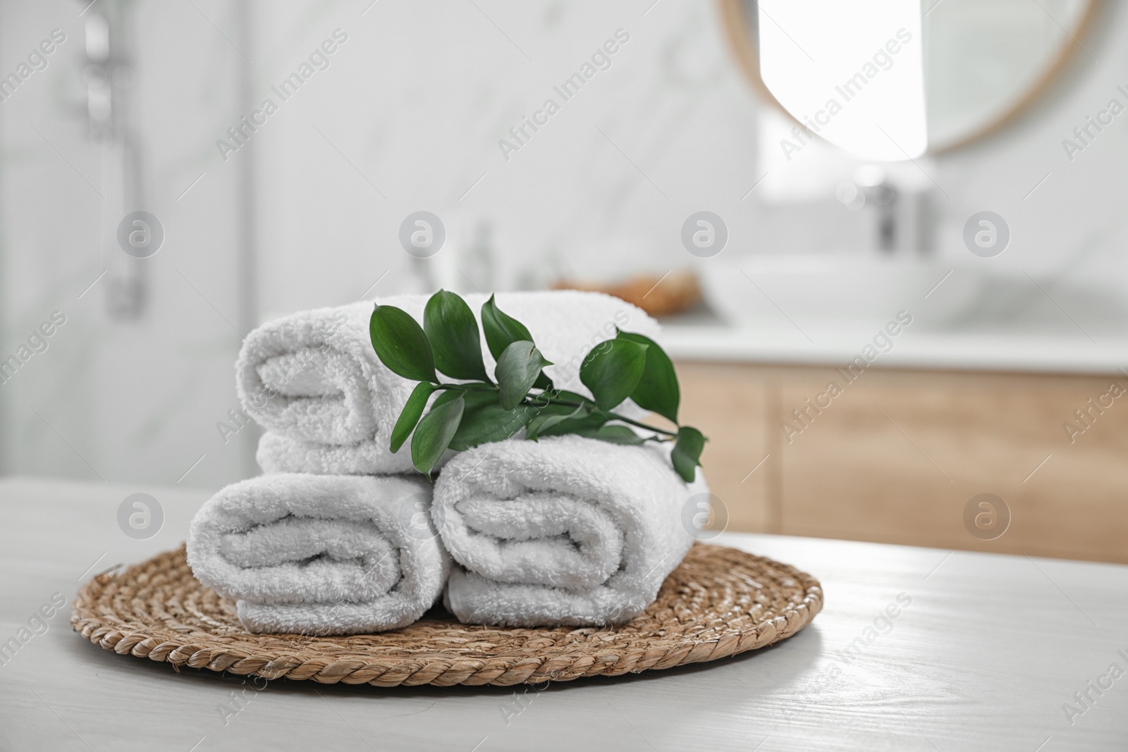 Photo of Rolled fresh towels and green leaves on white table in bathroom