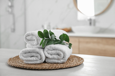 Rolled fresh towels and green leaves on white table in bathroom