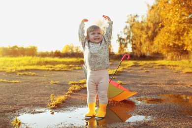Little girl wearing rubber boots standing in puddle outdoors, space for text. Autumn walk